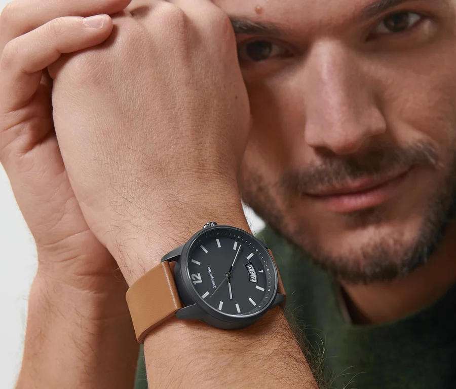 Mann schaut in die Kamera und trägt eine schwarze Armbanduhr Pilot Style Date mit braunem Lederarmband am Handgelenk.