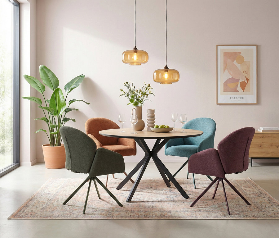 Ein modernes Esszimmer mit einem runden Holztisch und vier gepolsterten Stühlen in Dunkelgrün, Terrakotta, Hellblau und Pflaume. Zwei bernsteinfarbene Glaspendelleuchten hängen über dem Tisch, der mit einer Blumenvase, einer Schale mit grünen Äpfeln und Weingläsern dekoriert ist. Eine große Pflanze steht an einem Fenster, und ein gemusterter Teppich bedeckt den Boden.