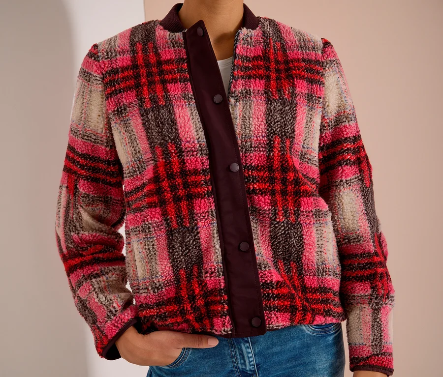 Person trägt einen CECIL Blouson aus flauschigem Material mit rot-rosa-beigem Karomuster und dunkler Knopfleiste, dazu blaue Jeans.