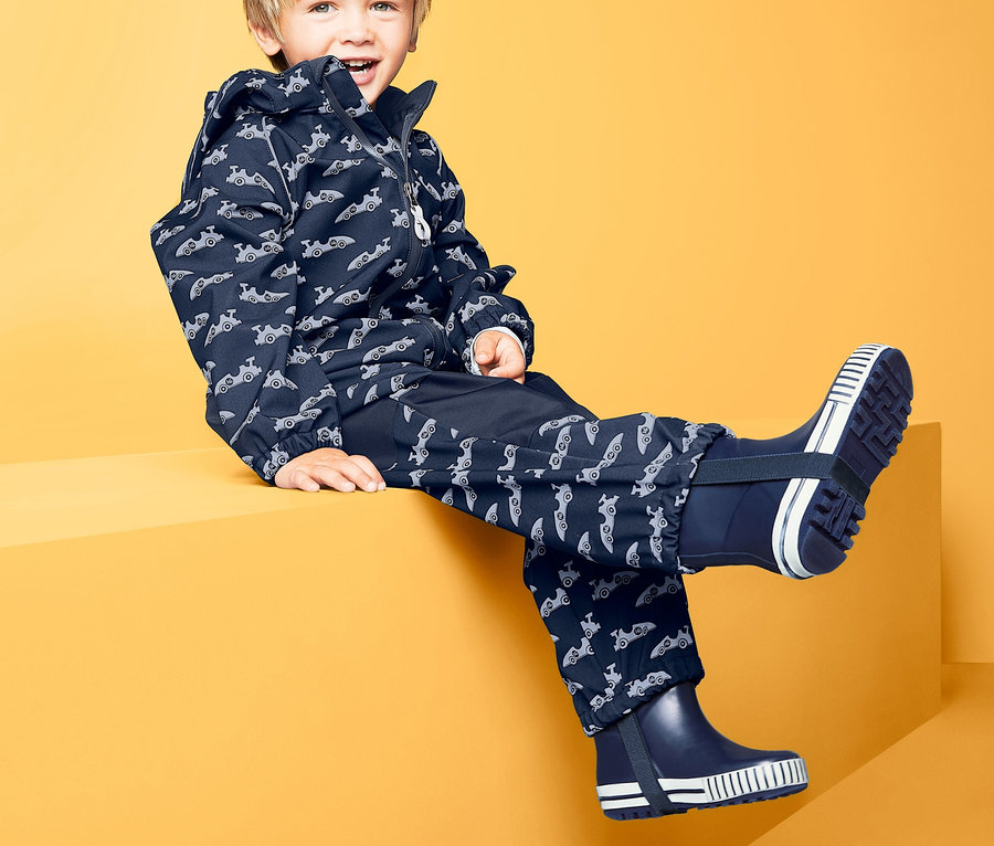Junge sitzt auf gelbem Block in Softshell-Overall.