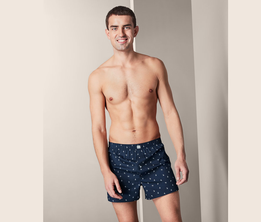 Lächelnder Mann trägt 2 Web-Boxershorts mit Ankerdruck.