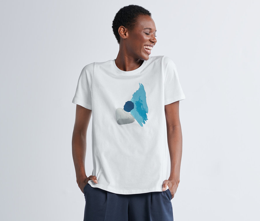 Frau lacht mit Händen in den Taschen, sie trägt ein T-Shirt mit Print.