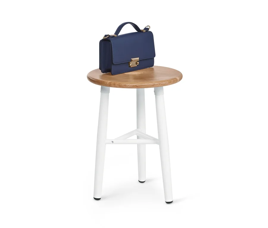 Blaue Handtasche auf einem dreibeinigen Hocker.