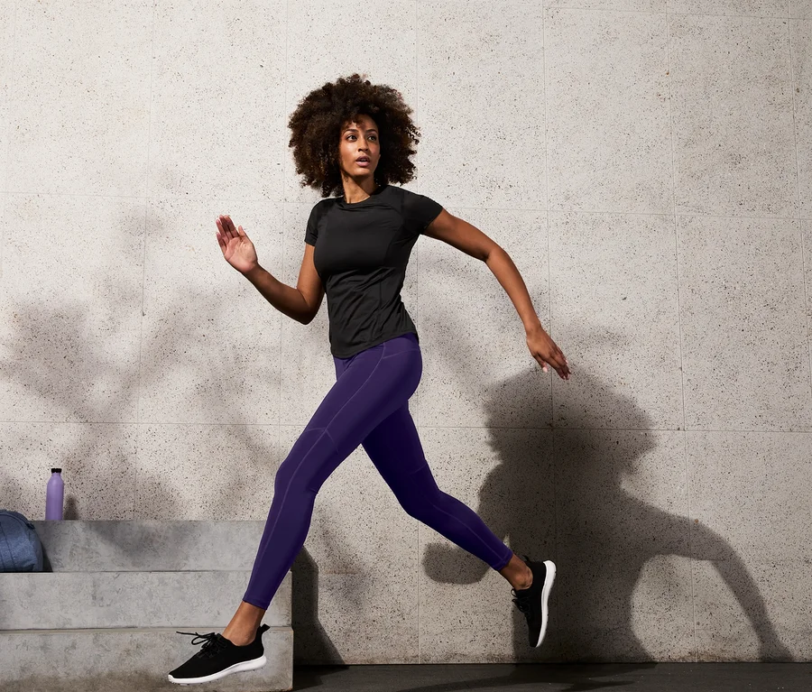 Frau in schwarzem Sportoberteil und Bodyforming-Sporttight beim Laufen.