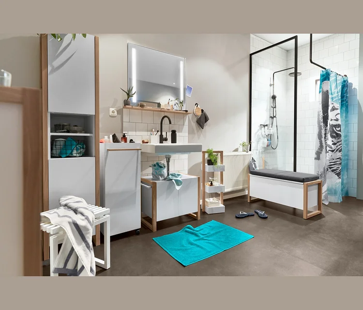 Badezimmer-Interieur mit Bad-Hochschrank, Waschbeckenunterschrank, Standregal mit 3 Stauraum-Kästen, Beistellwagen, Vogelgesangs-Box, Stauraumsitzbank, Duschvorhang, Badematte (türkis) und Bade-Zehentrenner.