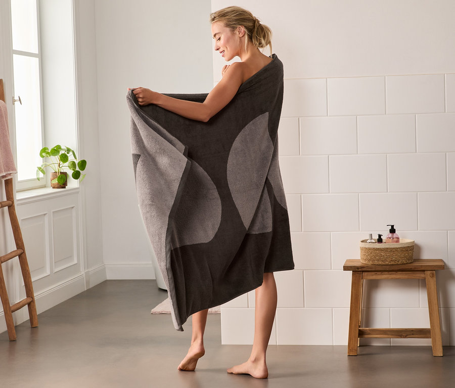 Frau hüllt sich im Badezimmer in ein braunes Premium-Badetuch XL.