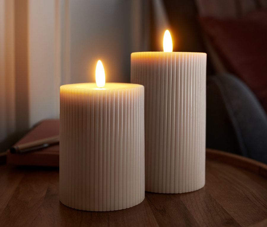 Zwei gerippte LED-Echtwachskerzen stehen auf einem Holztisch.
