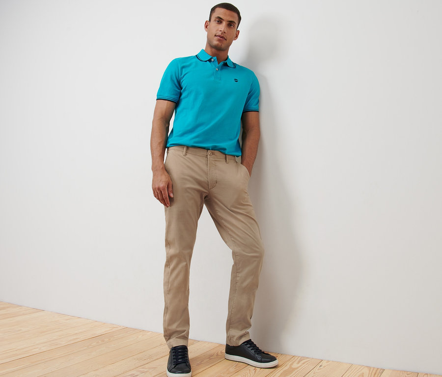 Mann posiert in beigen Chinos und blauem Poloshirt.