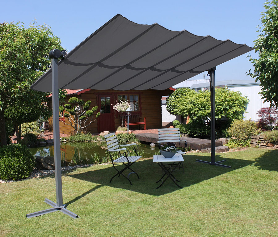 Eine anthrazitfarbene Leco Sonnenmarkise, 400 x 250 cm, steht auf einer Wiese und beschattet weiße Gartenmöbel.