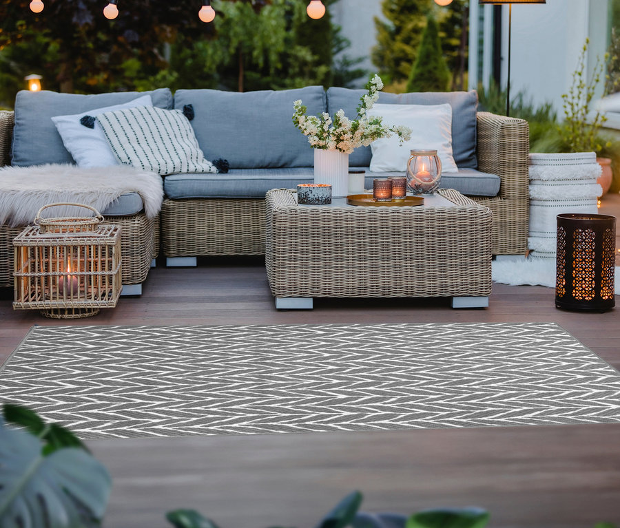 Außenbereich mit grauem Outdoor-Wendeteppich »Knitted Joy«, einer Korbgarnitur und Laternen.