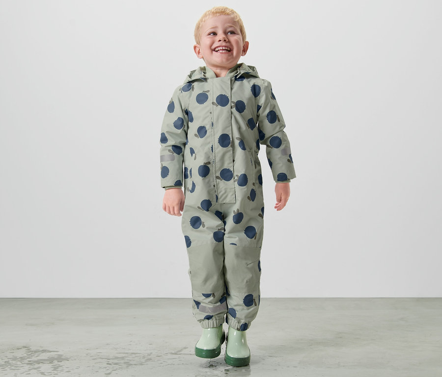 Ein Junge geht in einem Kleinkind-Regen-Einteiler.