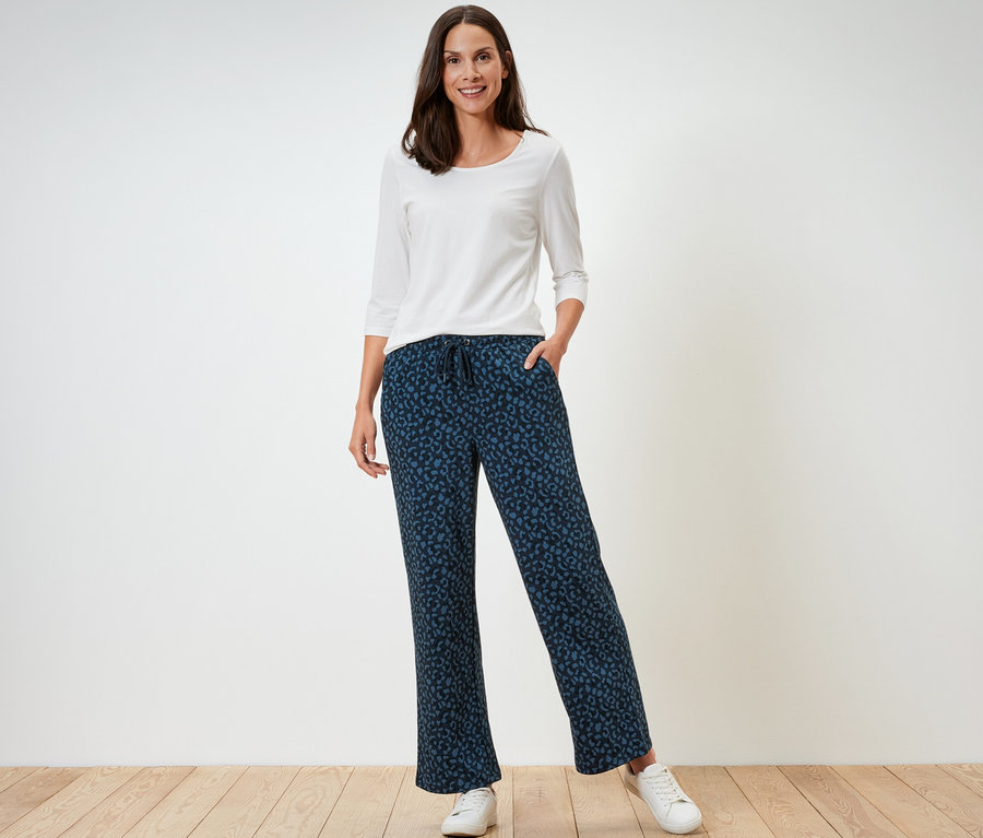 Eine Frau steht und trägt ein weißes Langarmshirt und eine bedruckte Sweathose.