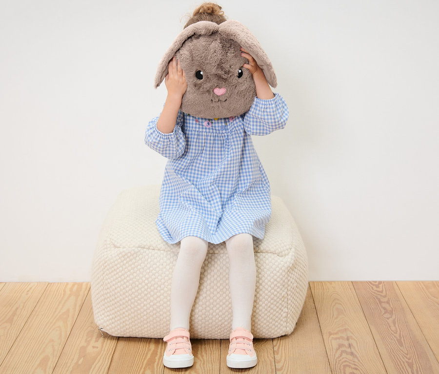 Mädchen sitzt auf einem Sitzsack und hält ein Häschen-Plüschkissen vor ihr Gesicht.