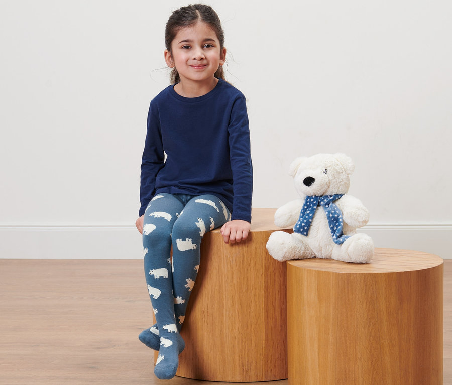 Mädchen sitzt auf einem Holzhocker und trägt 2 Kleinkind-Strumpfhosen mit Eisbärmuster.