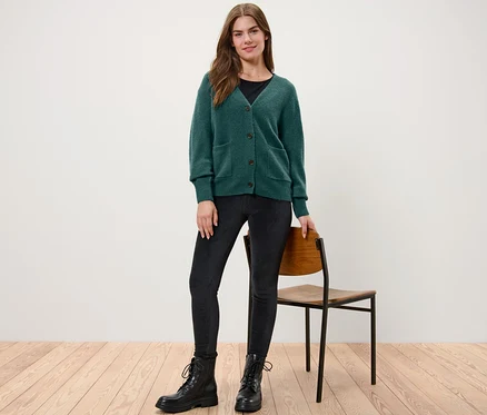 Frau steht und trägt eine dunkelgrüne Strickjacke mit Wolle.