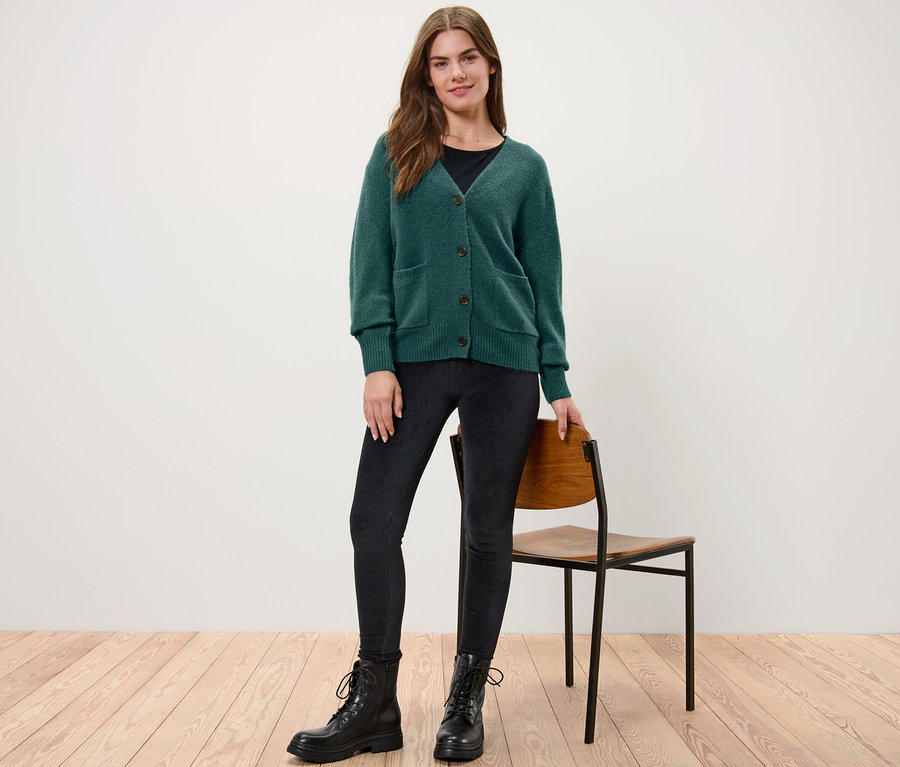 Frau steht und trägt eine dunkelgrüne Strickjacke mit Wolle.