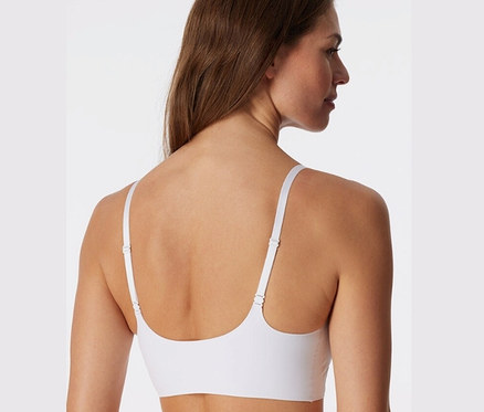 Rückansicht einer Frau mit braunen Haaren, die ein weißes, unsichtbares SCHIESSER Bustier mit Pads trägt.