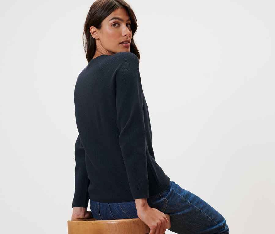 Frau sitzt auf einem Holzstuhl und trägt einen dunkelblauen Strickpullover.