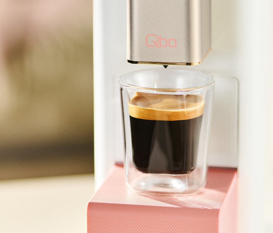 Qbo ICONIC x Pantone Special Edition Muted Clay Kaffeemaschine füllt eine Tasse mit Kaffee.