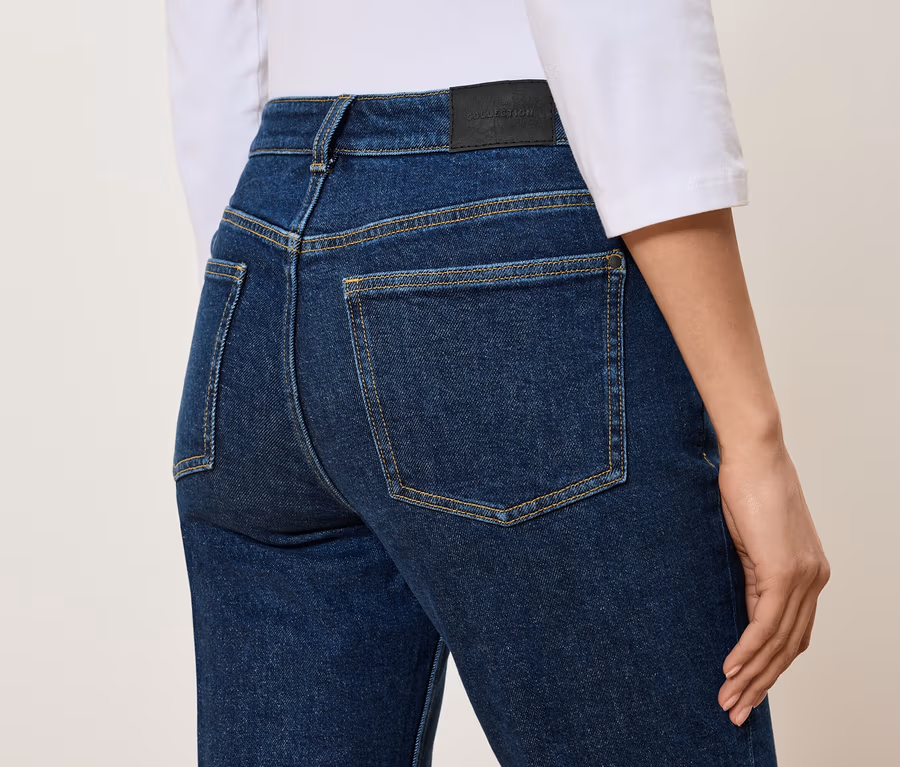 Rückansicht einer Frau in hochgeschnittenen, blauen Jeans und einem weißen T-Shirt.