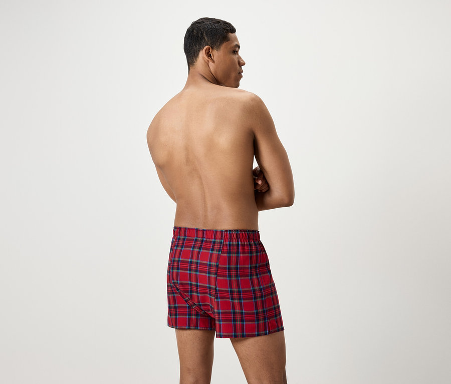 Mann mit dem Rücken zur Kamera trägt rote karierte Boxershorts.