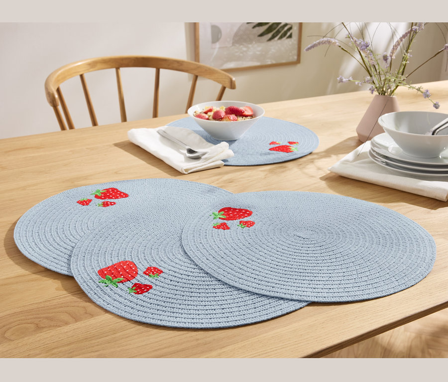 Vier blaue Platzsets mit Erdbeeren auf einem Holztisch.