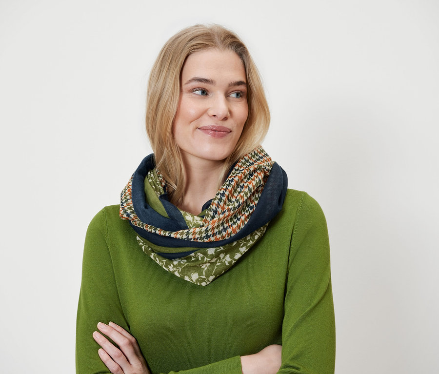 Blonde Frau trägt einen mehrfarbigen Schal und einen grünen Pullover.