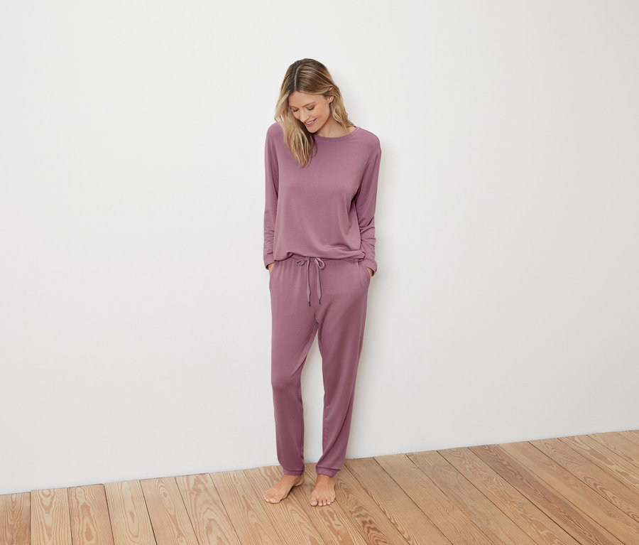 Frau im rosa Pyjama steht auf Holzboden.