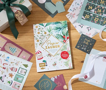 Dekorative Papiere, Aufkleber und eine Geschenkbox mit Schleife auf einem Holztisch.