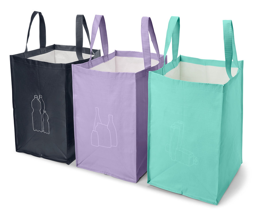 Drei Stoff-Einkaufstaschen stehen nebeneinander. Die Taschen sind dunkelblau, lila und hellblau und haben weiße Bilder von Recyclinggegenständen.