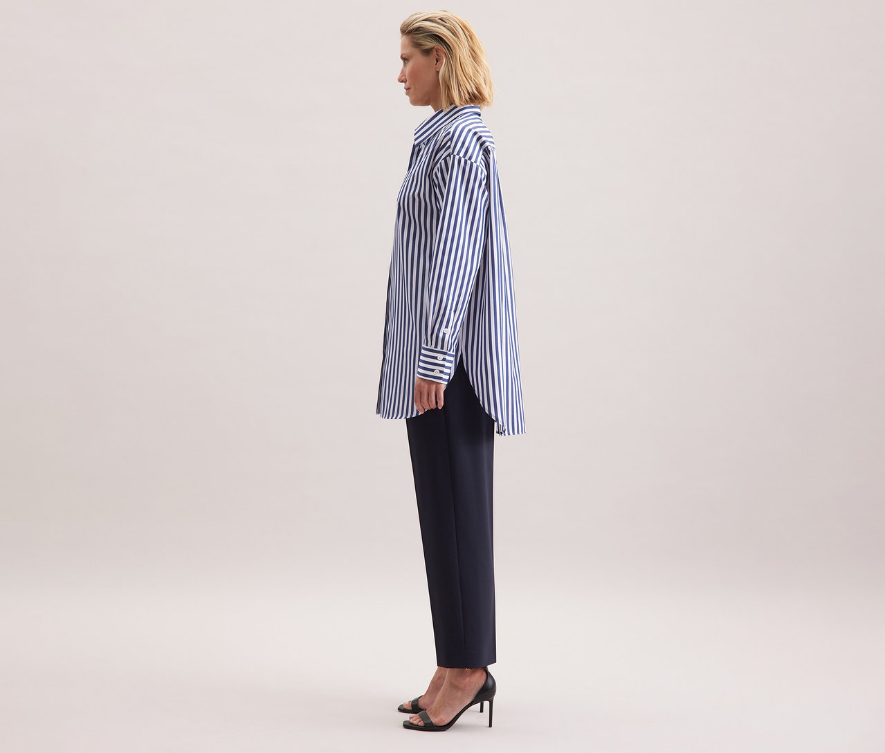 Frau trägt eine gestreifte Seidensticker Oversize Longbluse, dunkle Hose und schwarze Sandalen.