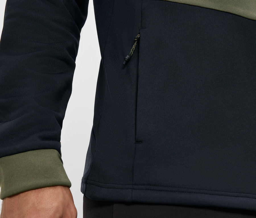 Detailaufnahme einer schwarz-olivgrünen Jacke mit Reißverschluss und Reißverschlusstasche.