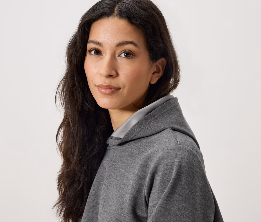 Porträt einer Frau mit langen, dunklen Haaren in einem grauen Kapuzenpullover.