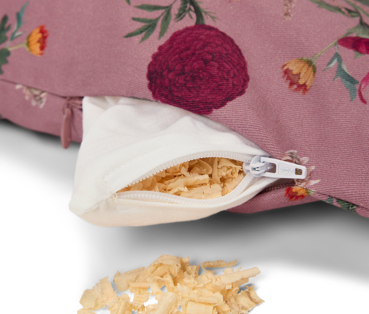 Detail eines lila Kissens mit Blumenmuster, mit offenem weißen Reißverschluss und Füllung aus Holzwolle.