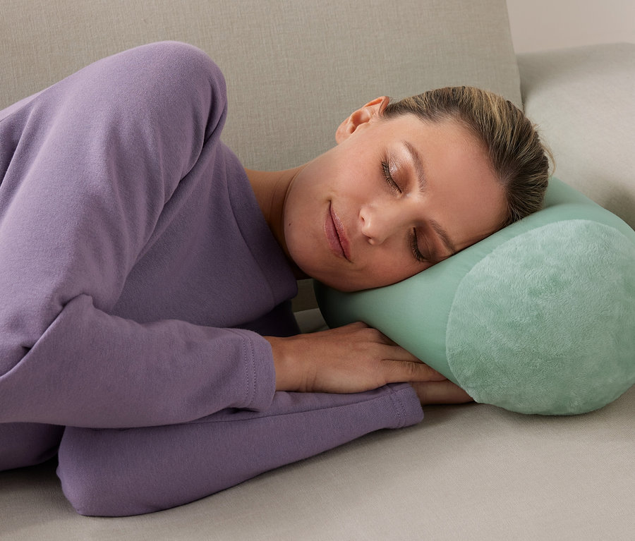 Frau schläft mit Relaxkissen auf Sofa.