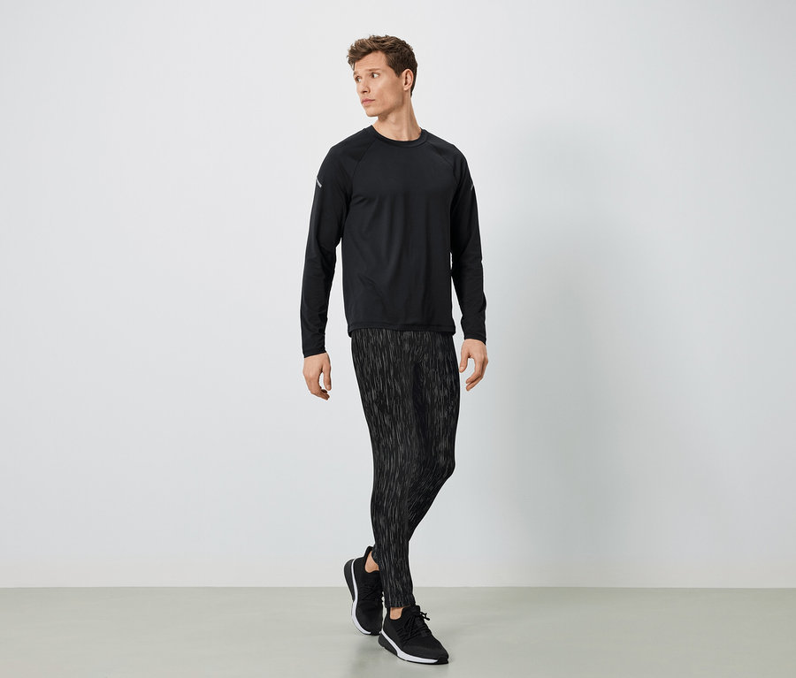 Ein Mann in schwarzer Sportbekleidung posiert vor hellem Hintergrund.