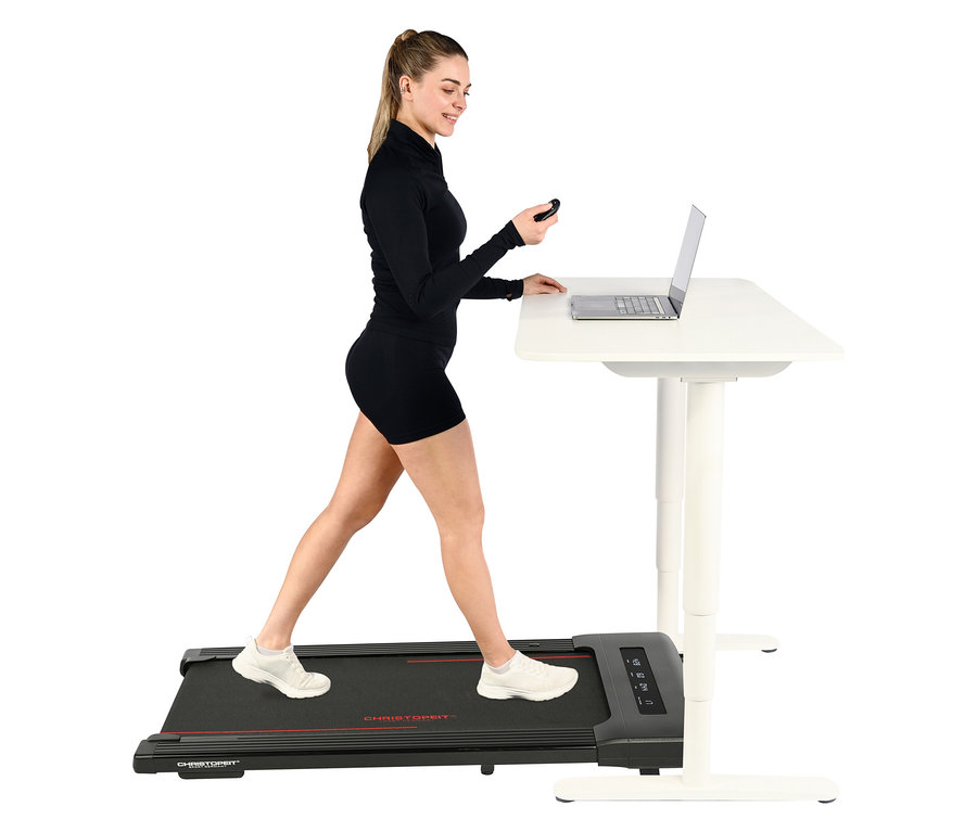 Frau geht auf Walking-Pad »4.1« neben einem weißen Schreibtisch mit Laptop.