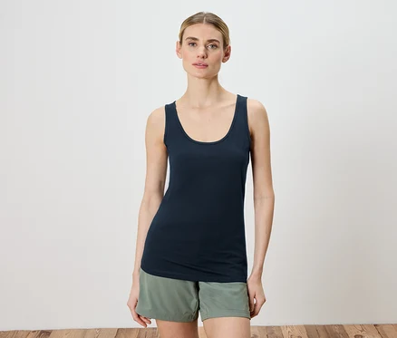 Frau trägt ein blaues Tanktop und grüne Shorts.