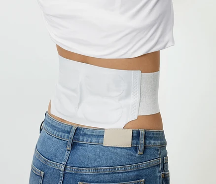 Eine Person trägt ein weißes Heizkissen um ihre Taille, zusammen mit einem weißen T-Shirt und blauen Jeans.