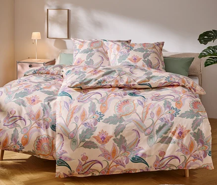 Ein Bett mit einer hellen Bettwäsche mit Blumenmuster steht in einem Schlafzimmer.