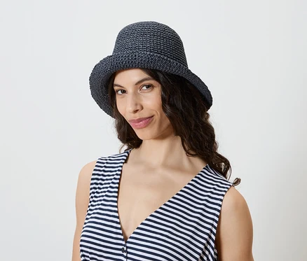 Frau mit dunklen, gewellten Haaren trägt einen marineblauen Häkelhut und ein gestreiftes Tanktop.