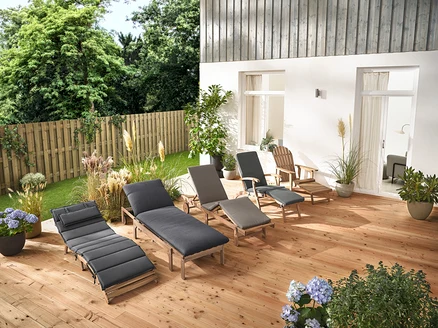 Mehrere Gartenliegen und ein Adirondack Gartensessel mit ausziehbarer Fußlehne aus Holz stehen auf einer Holzterrasse.