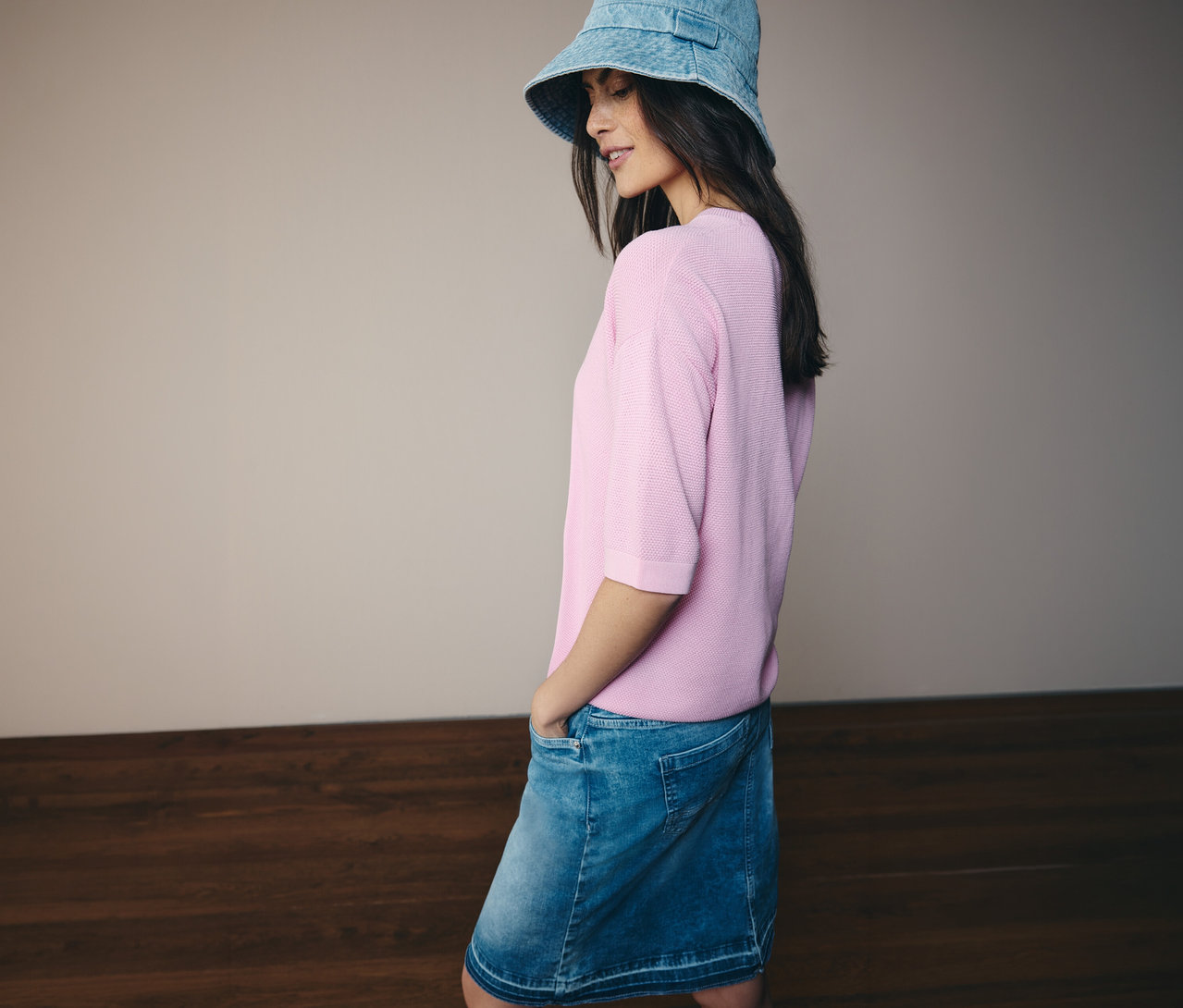 Frau mit Jeanshut, rosa CECIL Kurzarmpullover und CECIL Jeansrock. Sie hat die Hände in den Taschen.