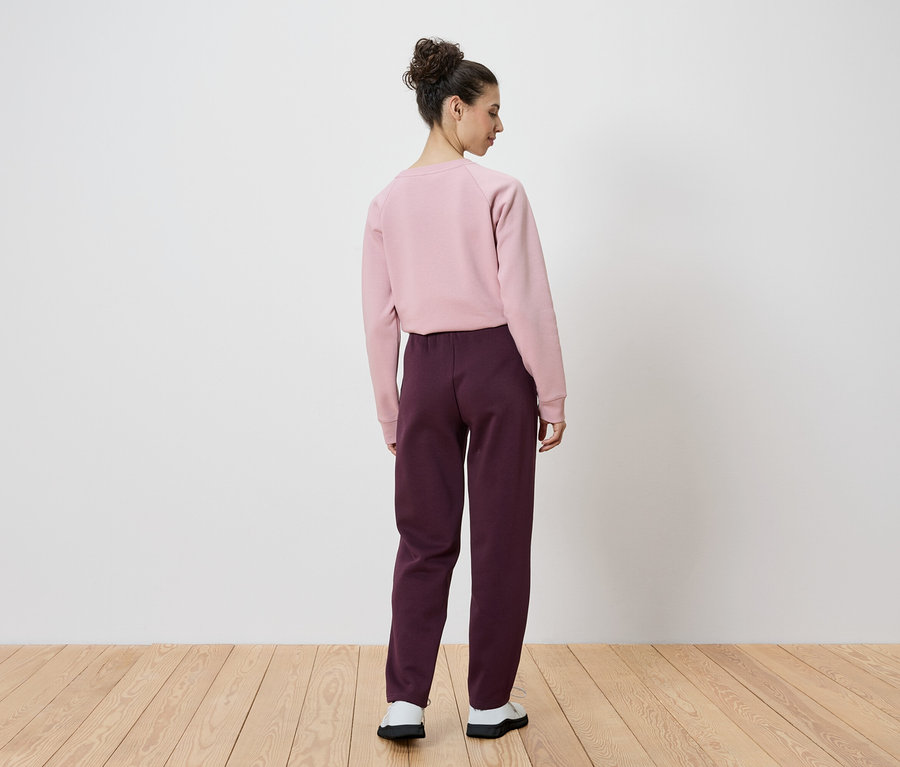 Rückansicht einer Frau mit Dutt, die ein rosa Sweatshirt und eine weinrote Hose trägt.