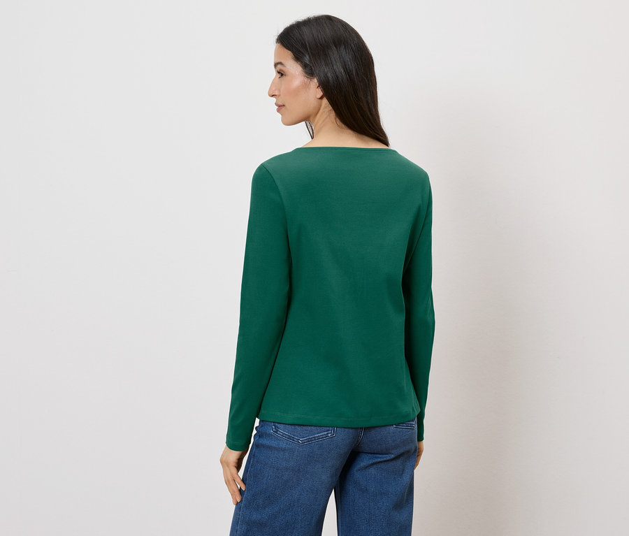 Eine Frau, von hinten gesehen, trägt ein grünes Langarmshirt und Jeans vor einem weißen Hintergrund.
