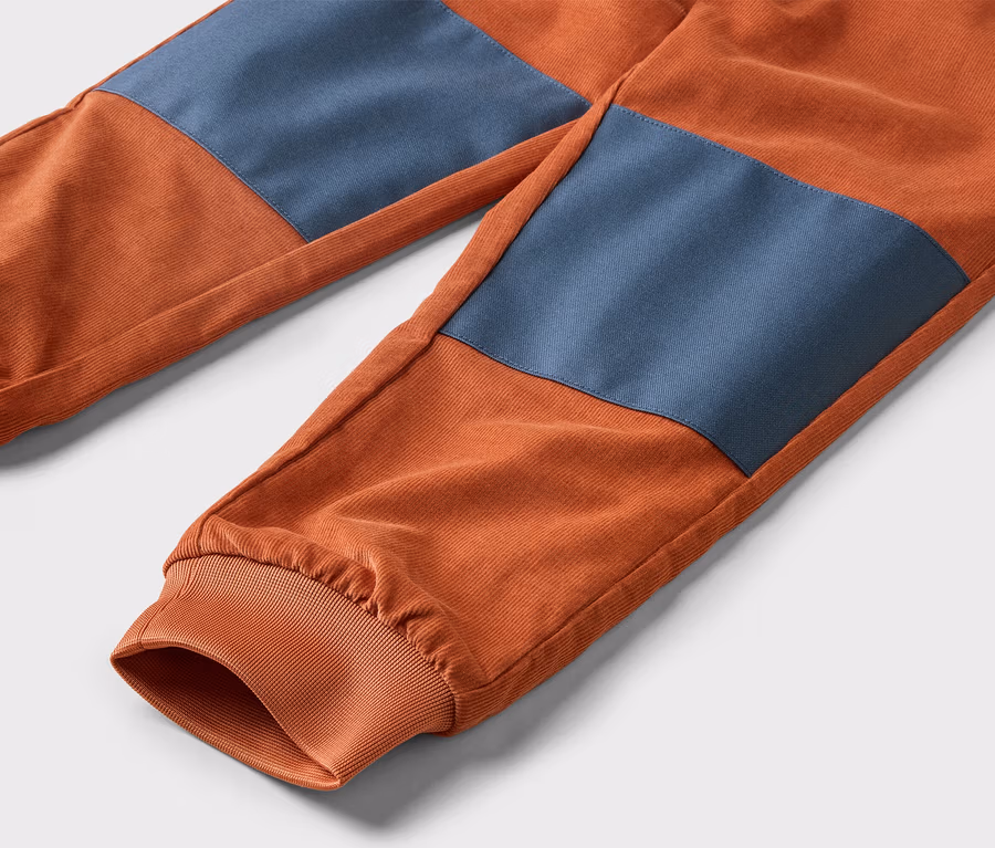 Nahaufnahme von orangefarbenen Cordhosen mit blauen Knieflicken und elastischen Bündchen an den Knöcheln.