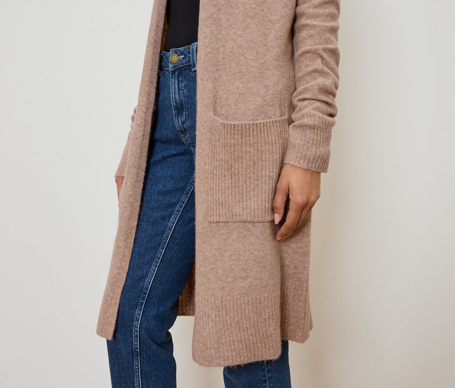 Nahaufnahme einer Frau, die eine lange, hellbraune Strickjacke mit Taschen und Jeans trägt.