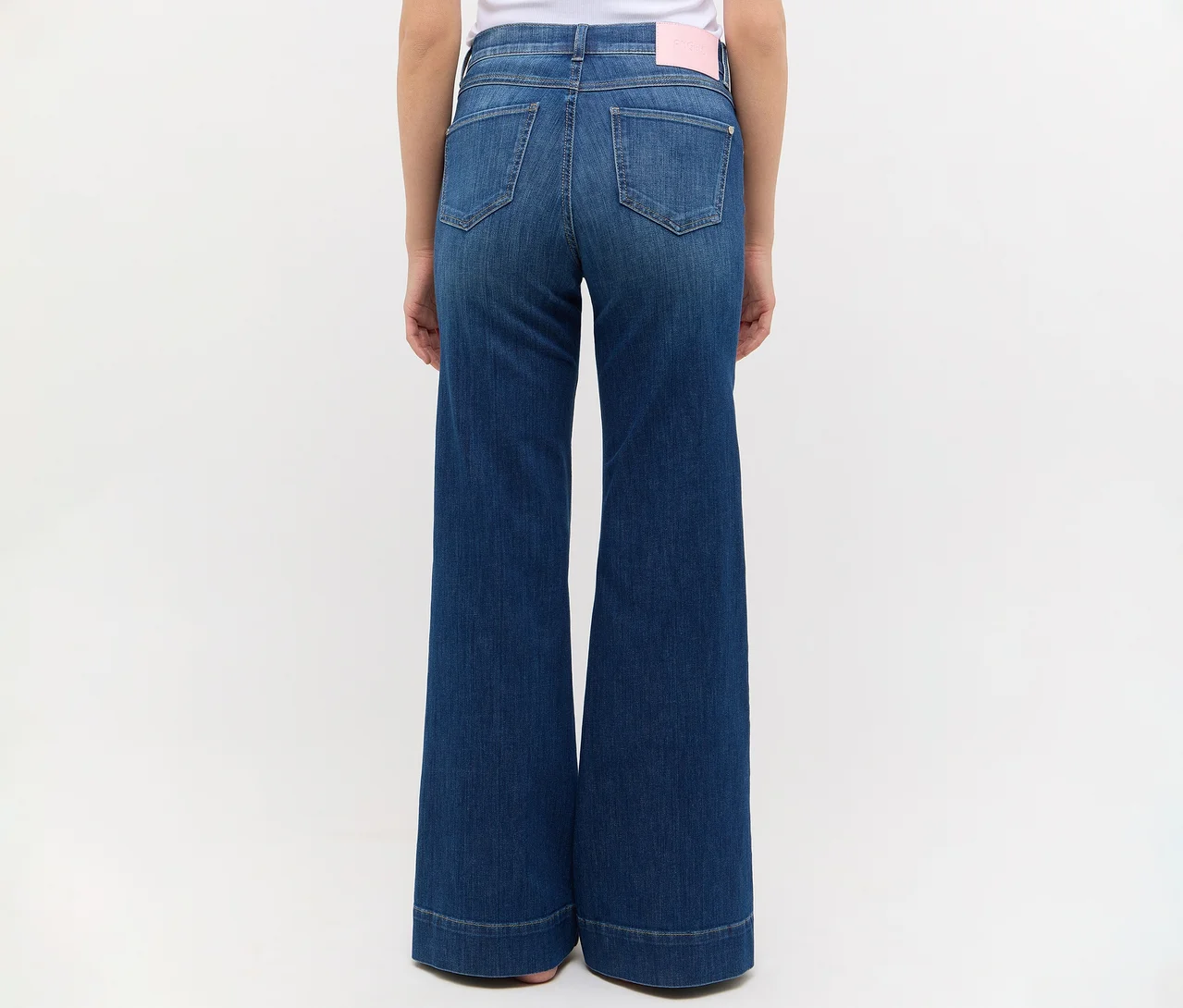 Rückenansicht einer Person in dunkelblauen, weit geschnittenen Jeans mit Gesäßtaschen und einem rosa Etikett am Bund.