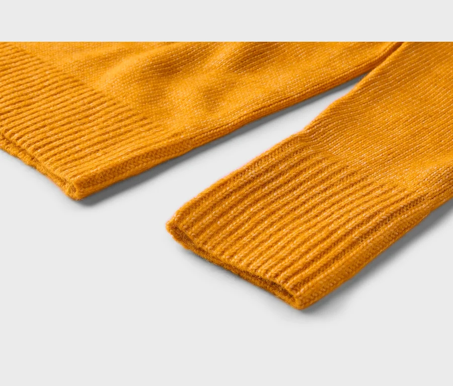 Nahaufnahme eines leuchtend gelben Strickstoffs, der einen gerippten Rand und ein geripptes Ärmelbündchen zeigt.
