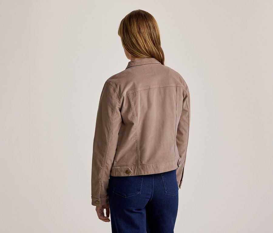 Frau von hinten gesehen, trägt eine hellbraune Jacke mit Kragen und sichtbaren Nähten sowie dunkelblaue Jeans.